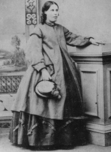 Margaret Gray, mulher grávida da Nova Zelândia, tenta disfarçar sua gravidez com um casaco largo na década de 1870.